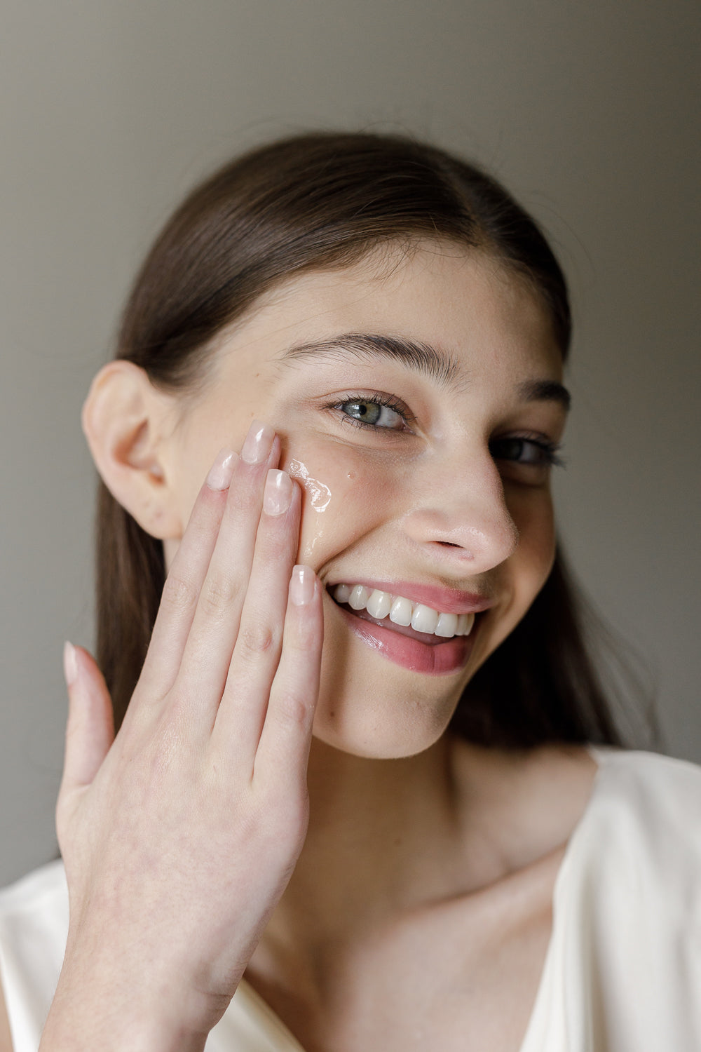 Woman applying Karee Hays Prebiotic Peptide Serum to her face with a neutral background