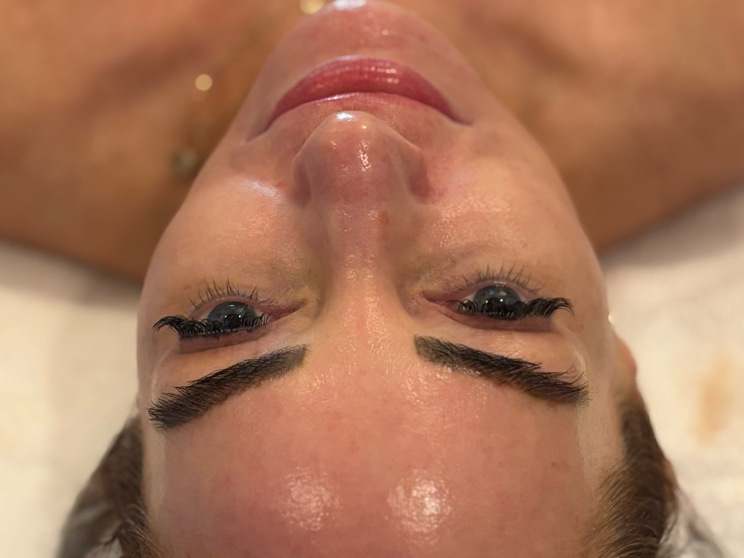 Close-up of a person's face with long, dark, defined eyebrows and black winged eyeliner, lying down on a treatment bed.