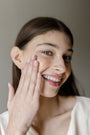 Woman applying Karee Hays Prebiotic Peptide Serum to her face with a neutral background