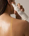 Person applying a skincare serum to their shoulder with KH Brand on the bottle.